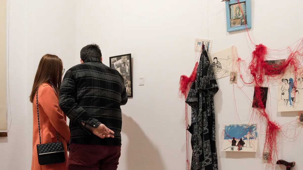 Two gallery visitors observing the Mamaia Vasilica installation closely